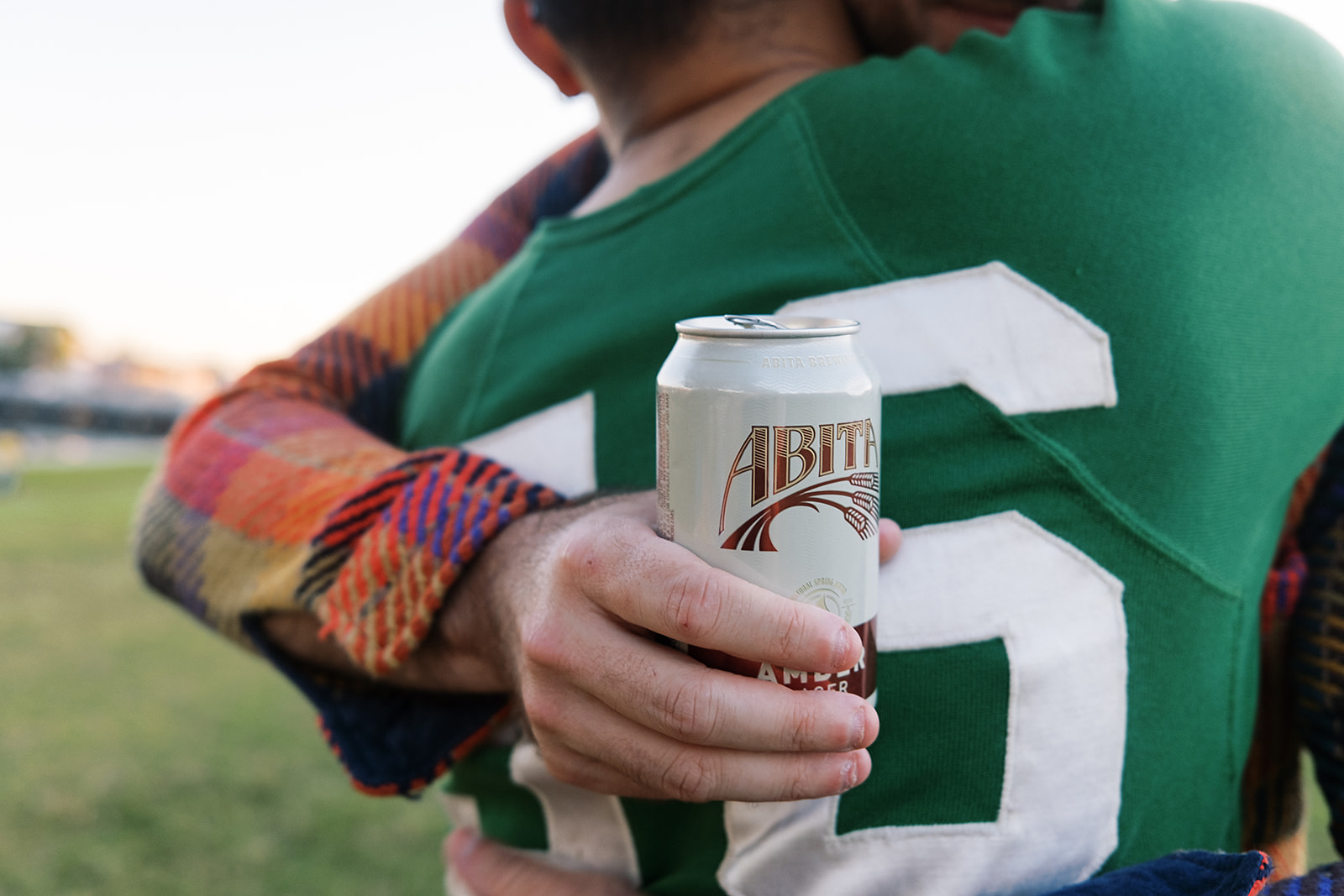 hugging while holding abita amber can in the park
