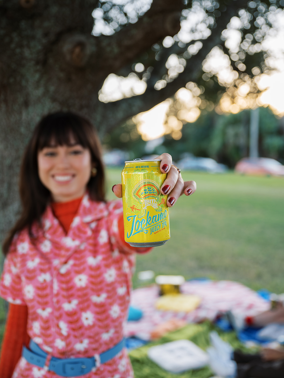 woman wearing fun jumpsuit holding a can of jockamo in the park