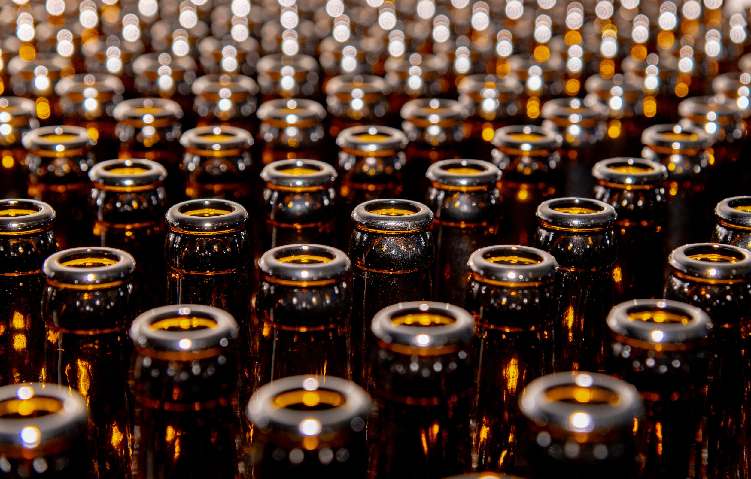 brown amber hued bottles lined up in a private label neutral malt base beverage manufacturing facility