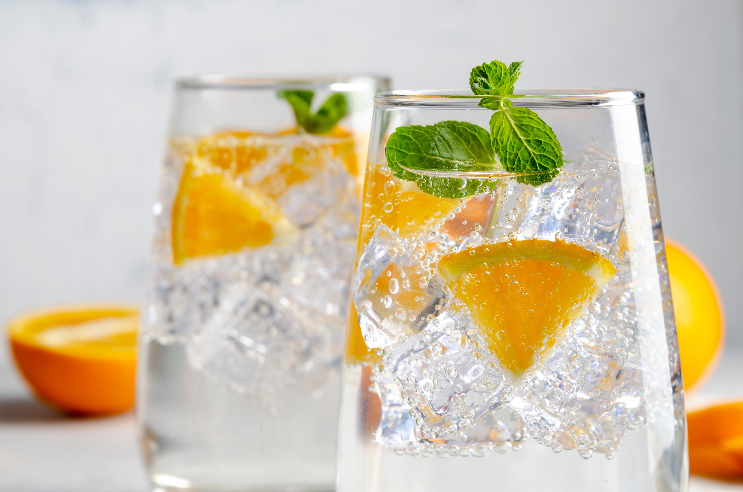 two clear glasses of private label hard seltzer with slides of orange in them and garnished with mint