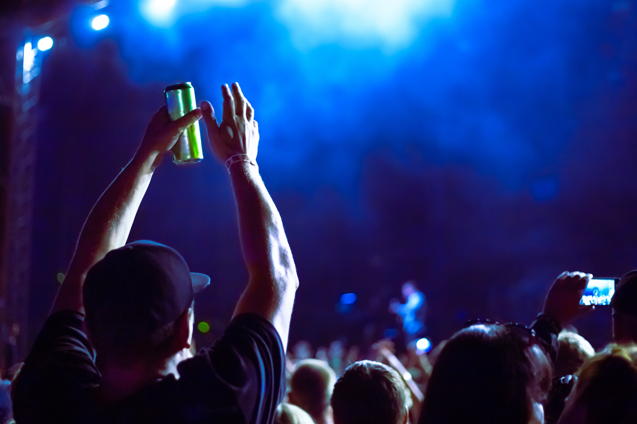 man at a concert holding his hands up in the air while holding a green can of beer