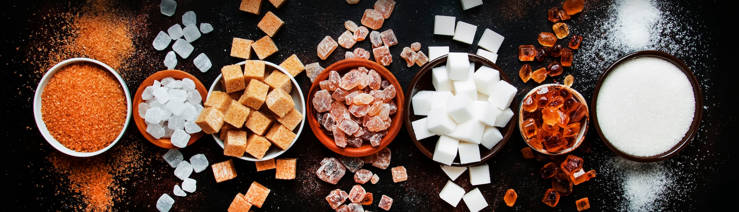 seven bowls containing a variety of types of sugar
