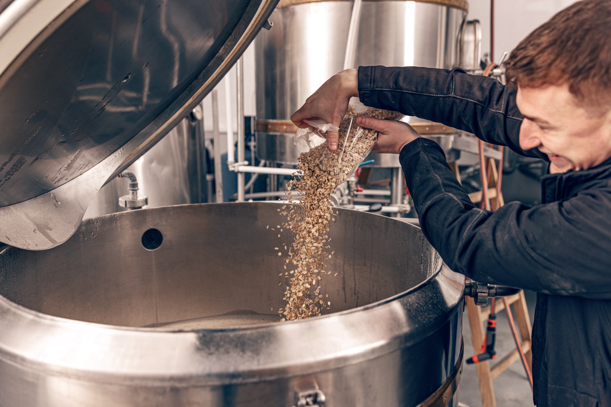 man pouring malt into a large stainless steel container