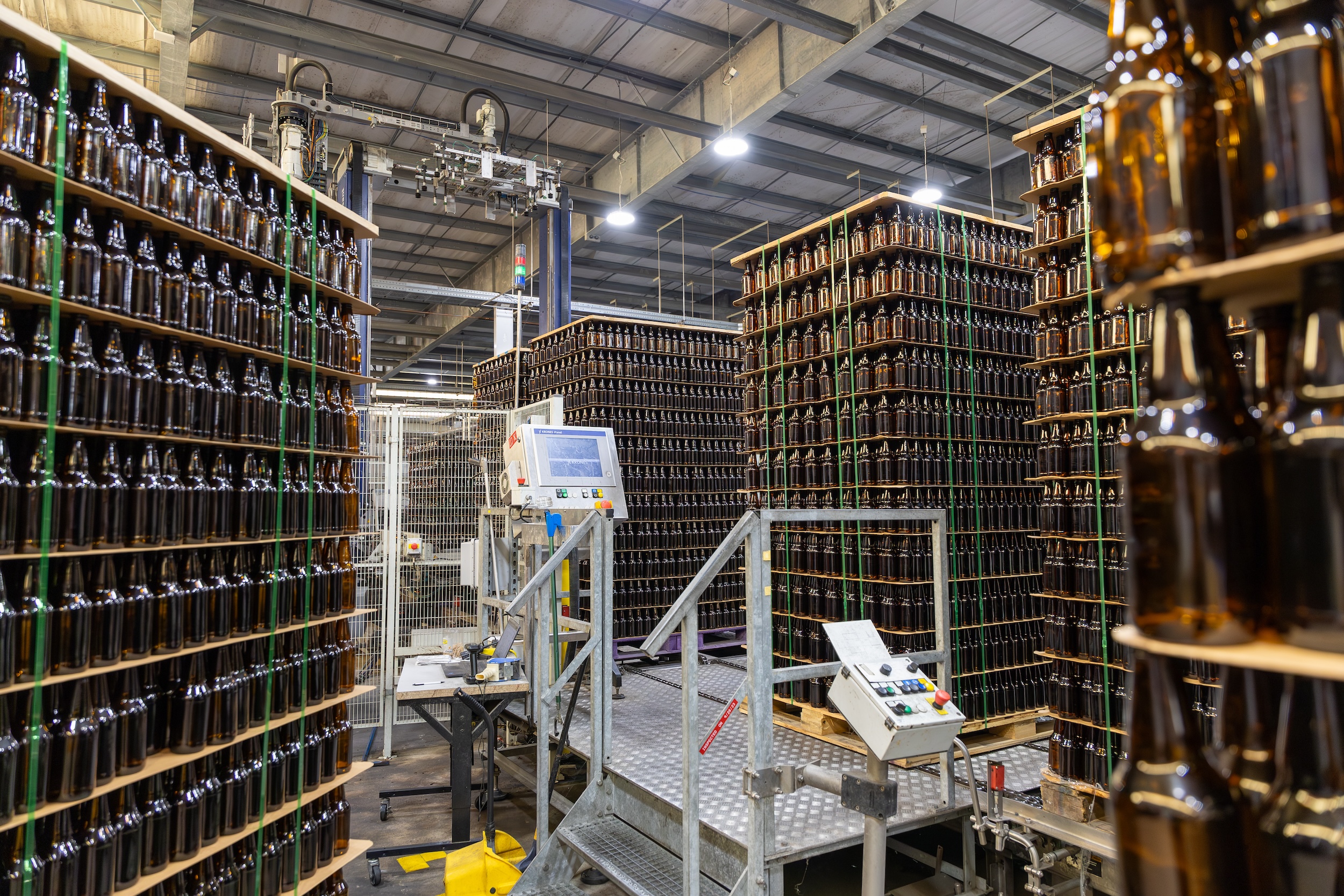 palettes of amber beer bottles stacked near to the ceiling in a beverage warehouse