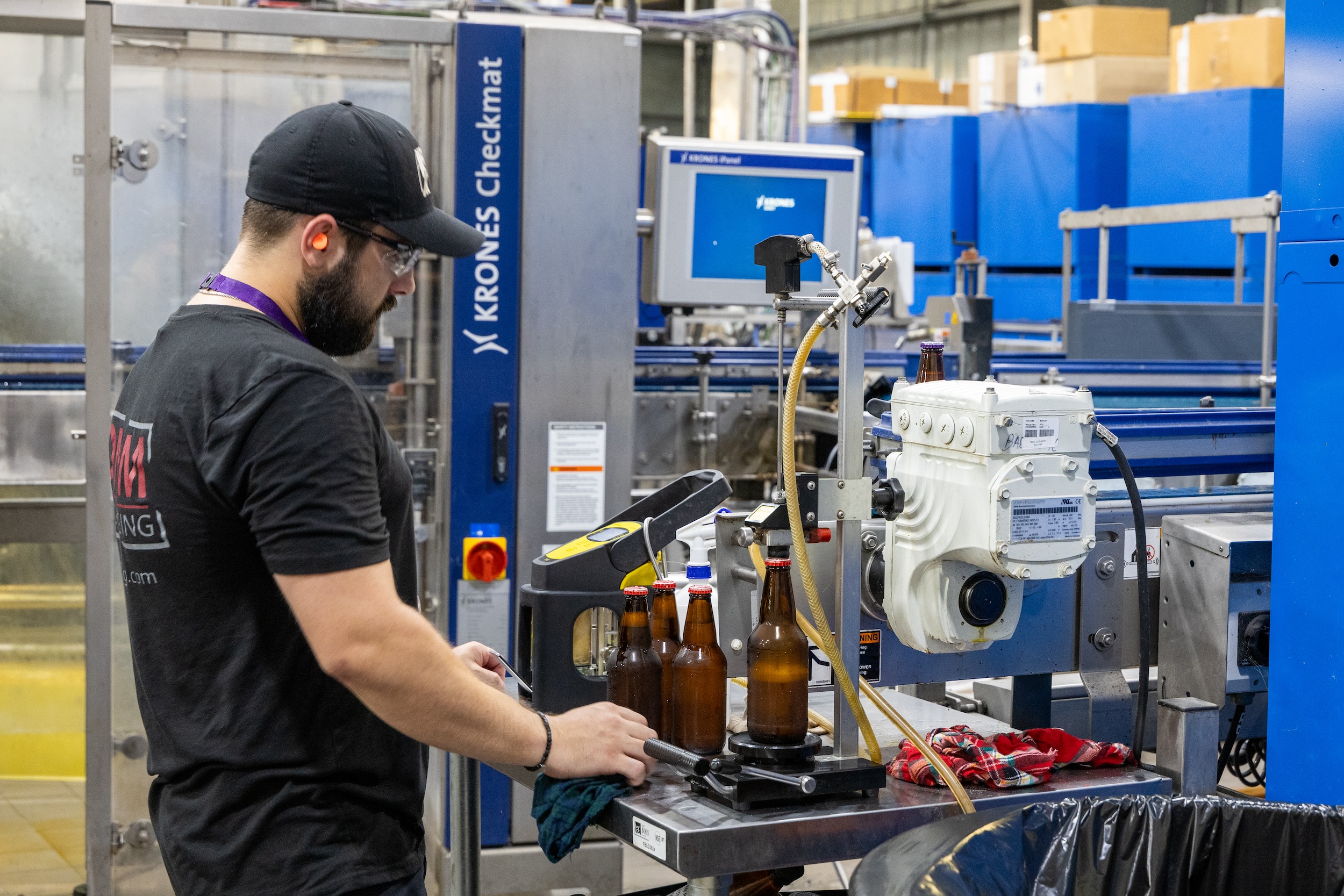man in a black baseball cap and wearing orange earplugs operating brewery equipment
